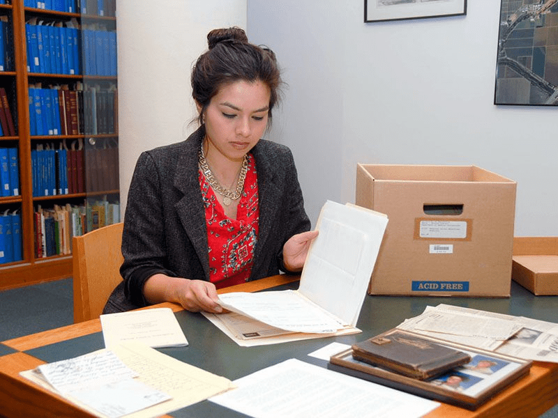 Student in red shirt and black blazer reading papers in a folder from the Library's special collections.